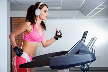 Fototapeta premium Fit girl with earphones running on treadmill in sports club