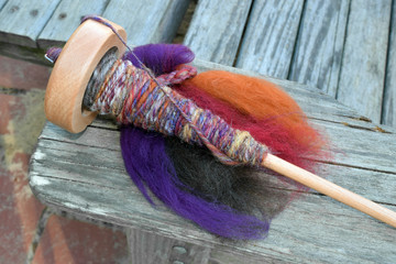 This is a photo of a drop spindle on a pile of colorful wool sheep roving. The spindle has handmade...