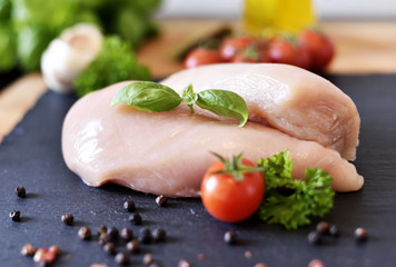 Raw chicken breast on a slate plate, with fresh cherry tomatoes, garlic and herbs. Cooking ingredients, healthy eating.