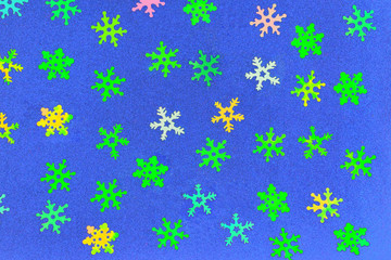 Abstract background from plastic snowflakes of different colors on a blue velvet paper