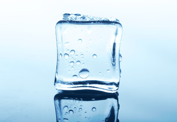 Transparent ice cube with reflection on blue glass with water drops