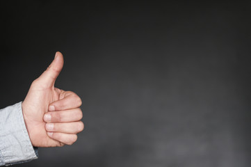 Hand mit Daumen nach oben / Positive Emotion, Hand mit Daumen hoch vor dunklem Hintergrund mit...
