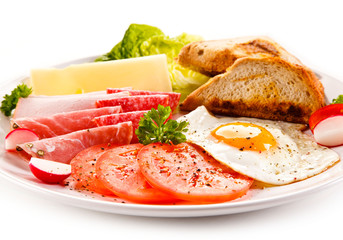 Breakfast - toasts, fried egg and sausages, cheese, ham and vegetables 