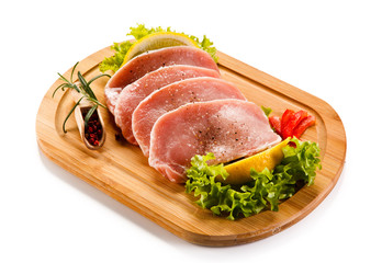 Raw pork chops on cutting board and vegetables 