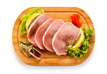 Raw pork chops on cutting board and vegetables 