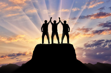 Silhouette of happy three climbers on the top of the mountain