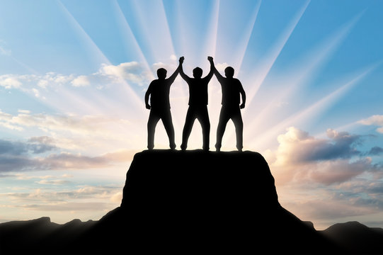 Silhouette of happy three climbers on the top