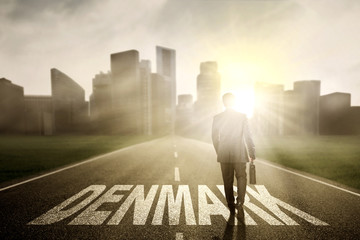 Fototapeta premium Businessman walking above Denmark word at sunrise