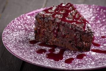 White tasty sweet sugar chocolate cake with pink jam on purple plate with white sugar powder