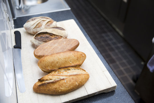 Different kinds of artisanal breads with a bread knife and cutting board in a restaurant kitchen in Amsterdam.