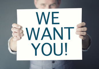 man holding sign with words We Want You