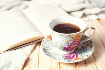 Cozy home still life: cup of hot coffee or tea and opened book with warm plaid