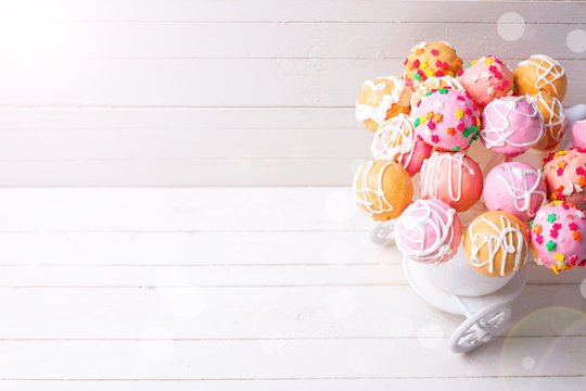Bright cake pops in ray of light   on white wooden background.