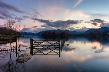 Dusk sunset at Derwentwater in the Lake District with flooded gate and fence.