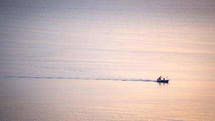 Fototapeta premium silhouette sunrise of minimal fishery boat sail on calm sea