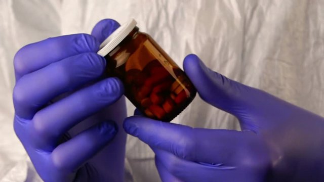 Forensic scientist examining unlabeled bottle of various pills and medication during crime scene investigation