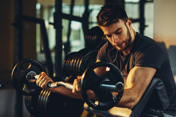 Handsome man doing biceps lifting barbell on bench in a gym - obrazy, fototapety, plakaty