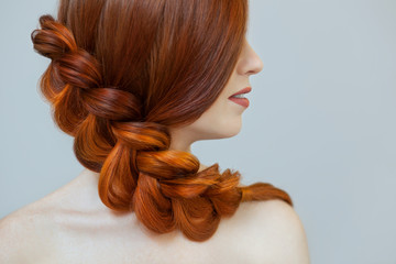 Beautiful girl with long red hair, braided with a French braid, in a beauty salon. Professional...