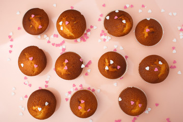 Muffins in paper forms and a lot of small sugar hearts on a mirrored background. Top view