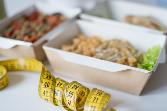 Вегетарианская еда в крафт коробках на заднем фоне с размытым фокусом, на переднем плане желтая сантиметровая лента в фокусе