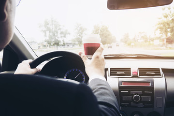 Man driving car while holding a cup of coffee