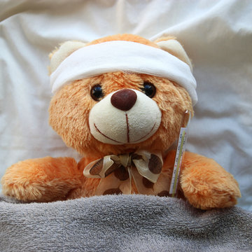 Teddy Bear with Bandage and thermometer lying in the bed