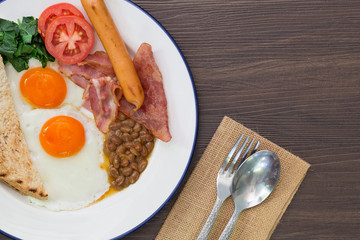 American breakfast in white dish with fork and spoon on brown wo