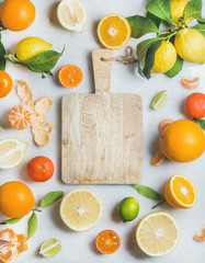 Variety of fresh citrus fruit for making juice or smoothie and wooden chopping board in center over light grey marble background, top view, copy space. Healthy eating, vitamin, clean eating concept