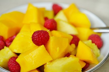A fresh fruit bowl with mango, raspberries and pineapple chunks