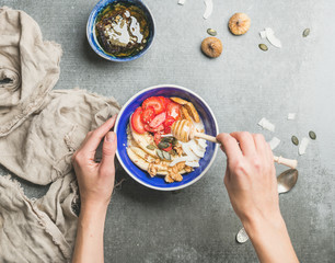 Yogurt, granola, seeds, fresh and dry fruits and honey in blue ceramic bowl in woman' s hands over grey concrete background, top view. Clean eating, detox, dieting, vegetarian food concept