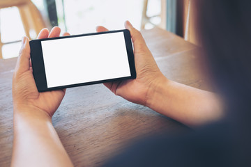 Mockup image of hands holding black mobile phone with blank white screen on vintage wood table in cafe