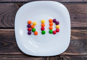 White plate with colorful sweet kids candies on dark wooden table. Children menu. Sweet word.