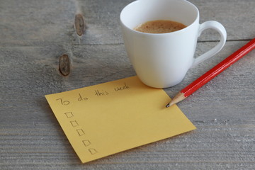 Yellow to do list with coffee and red pencil on wood background