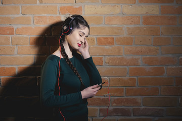 Woman in earphones listen music at brick wall in dark room