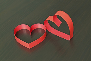 Two red hearts made of paper strips on a black wooden background