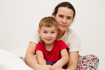 mother with  little son dressed in pajamas are relaxing and playing in the bed at the weekend together, lazy morning.