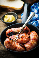 Sausages with prunes and bacon in iron pan