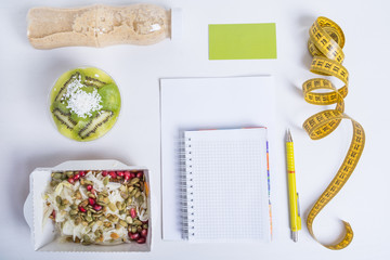 План здорового питания на день для одного человека. Блюда в крафт коробках, блокнот, ручка, визитка, сантиметровая лента и деток-вода на белом фоне.