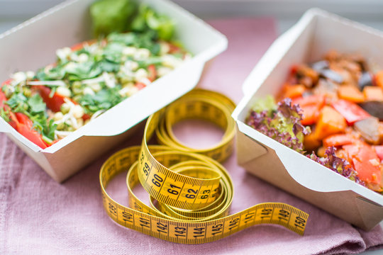 сантиметровая лента на переднем плане в фокусе, на заднем плане 2 диетических вегетарианских блюда на льняной салфетке. Здоровый план питания.
