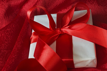 Gift in white packaging red ribbon tied on a red cloth