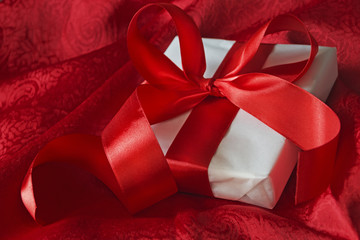 Gift in white packaging red ribbon tied on a red cloth