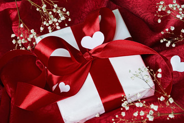 Gift in white packaging red ribbon tied on a red cloth. White fl