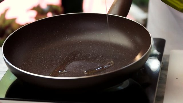 Oil slowly pouring in pan. Frying pan and electric stove.