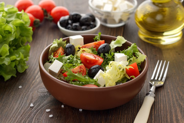 Bowl of fresh salad with feta and olives on wooden rustic table.