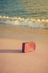 Retro suitcase, open water and sandy beach outdoors background