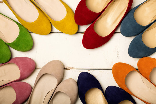 Row of colorful shoes (ballerinas) on a white wooden background.