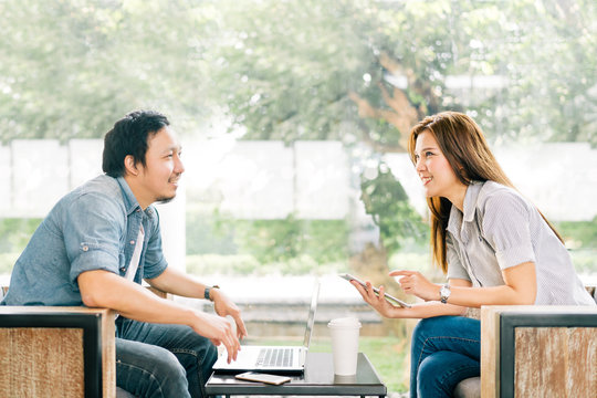 Young Asian couple or coworker talking at coffee shop or modern office, garden background. With laptop notebook, smartphone and digital tablet. Modern lifestyle with computer gadget technology concept
