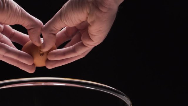 Hand cracks fresh egg in the glass bowl
