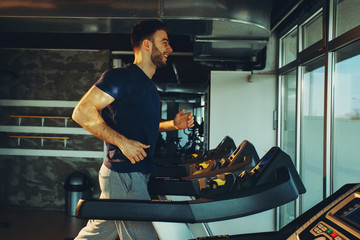 Young handsome man in sportswear running on treadmill at gym