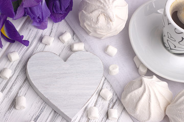 Still life with cup of coffe marshmallow zephyr iris flowers heart sign on white wooden background.